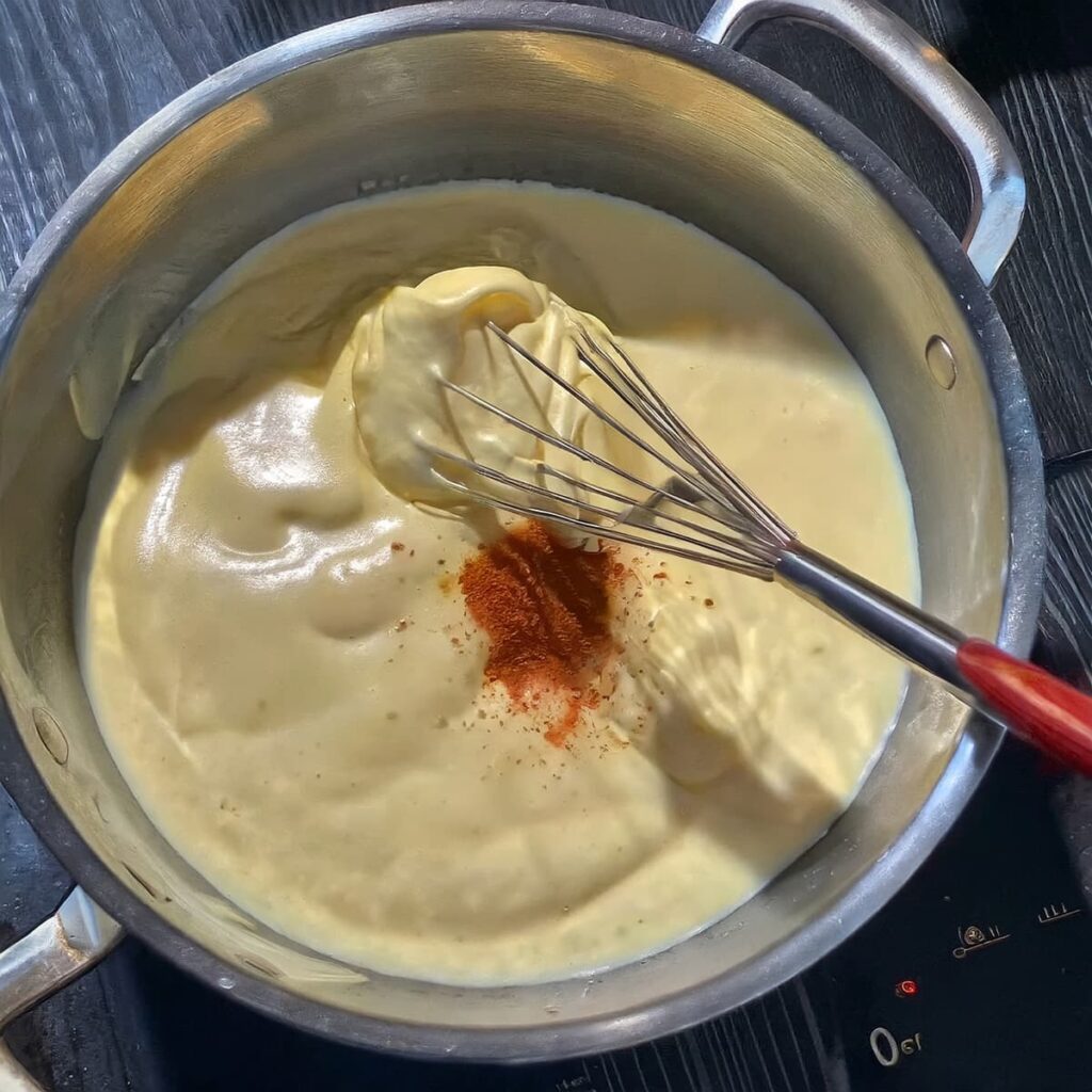 Gesmolten kaassaus in een pan met snuf cayennepeper