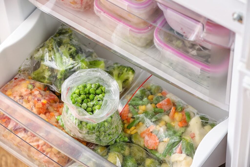 Plastic zakken met bevroren groene erwten en verschillende groenten in de koelkast