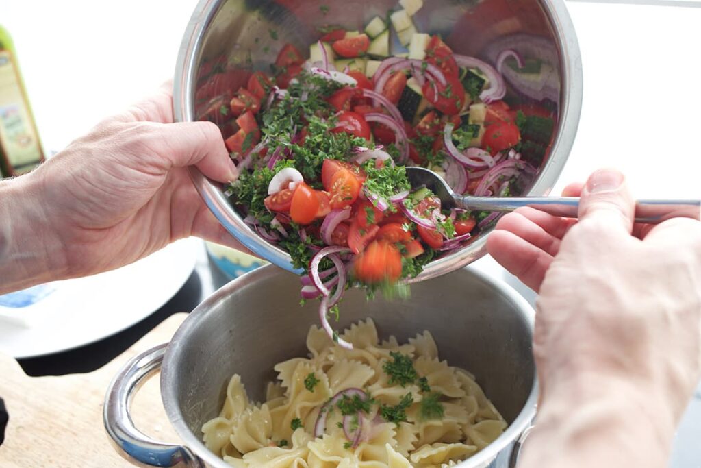 Voeg de gesneden ingrediënten toe en maak de Griekse pastasalade met feta.